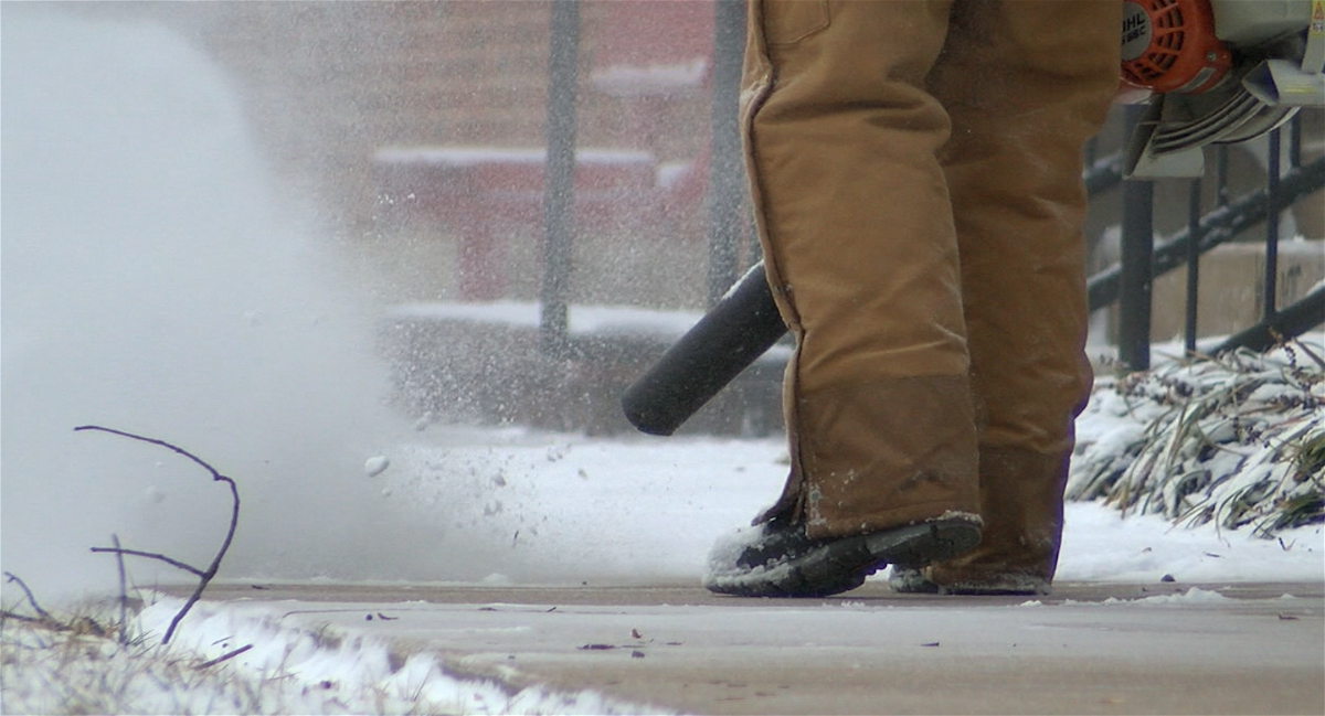A Jefferson City man uses a leaf blower to clear a layer of snow off of a sidewalk on Monday.