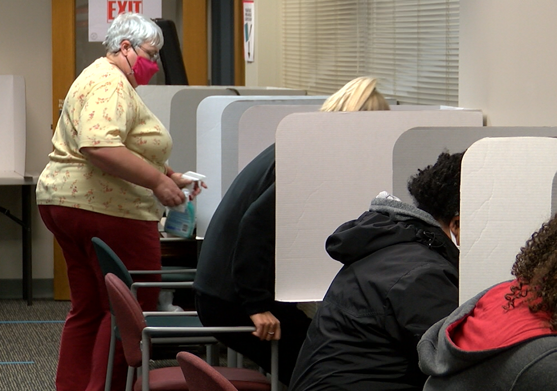 A woman sanitizes a voting booth in the Boone County Clerk's Office