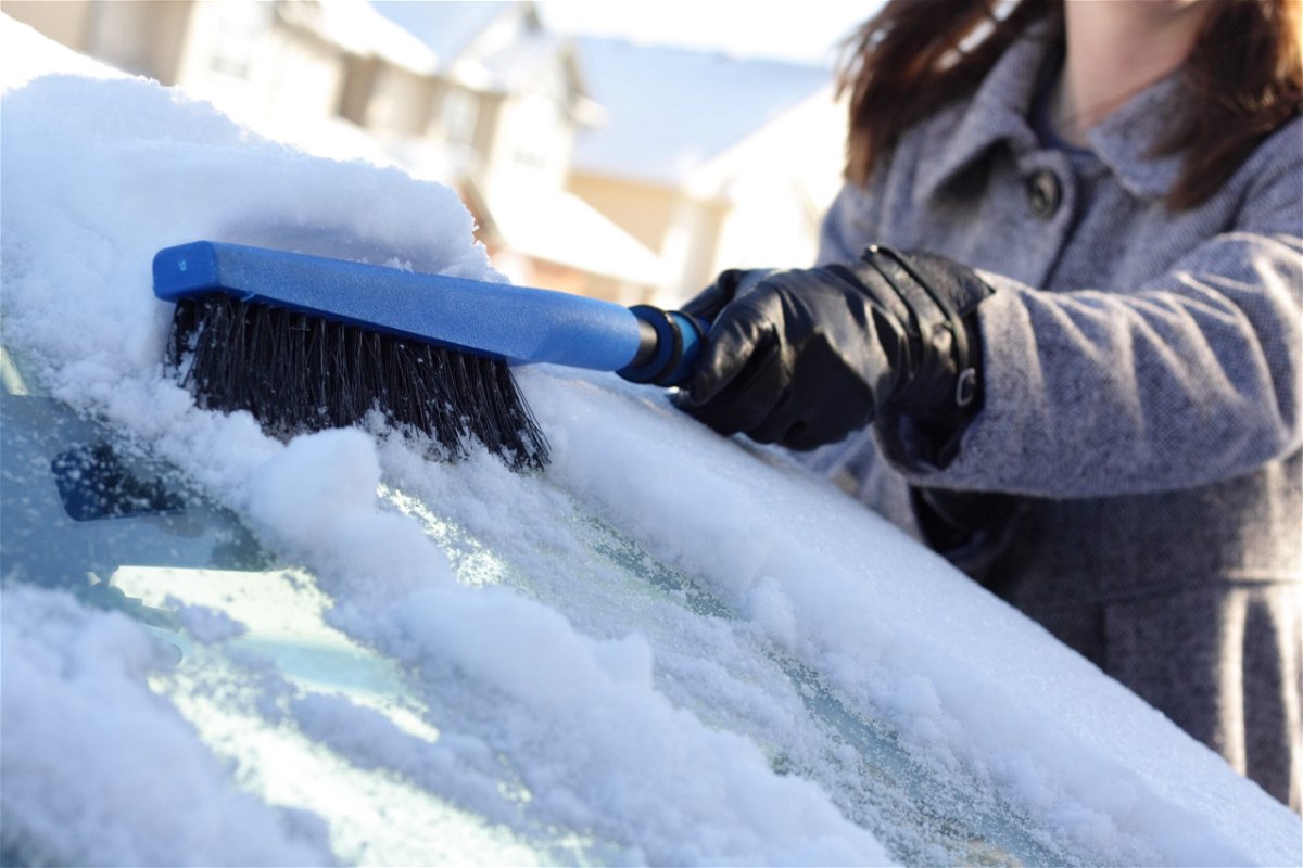 A woman brushes snow off of her car.