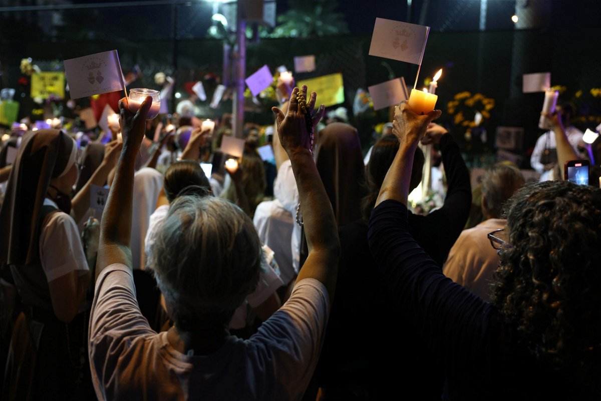 <i>Anna Moneymaker/Getty Images</i><br/>People lift their hands during a  prayer at the memorial site for victims of the collapsed condo building.