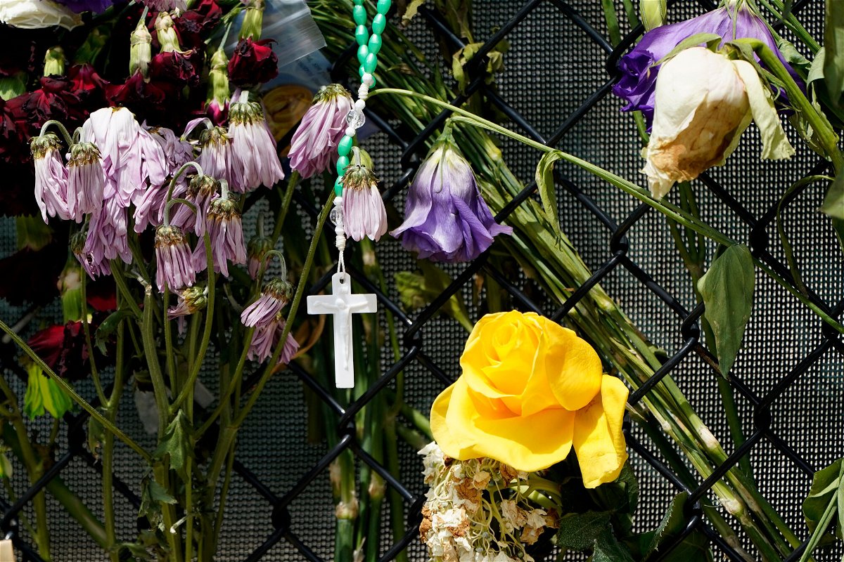 <i>Lynne Sladky/AP</i><br/>A cross hangs among wilting flowers at a makeshift memorial near the Champlain Towers South condo building.