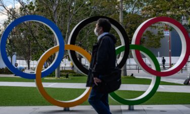 A man wearing a face mask walks in front of the Olympic Rings in Tokyo on March 11