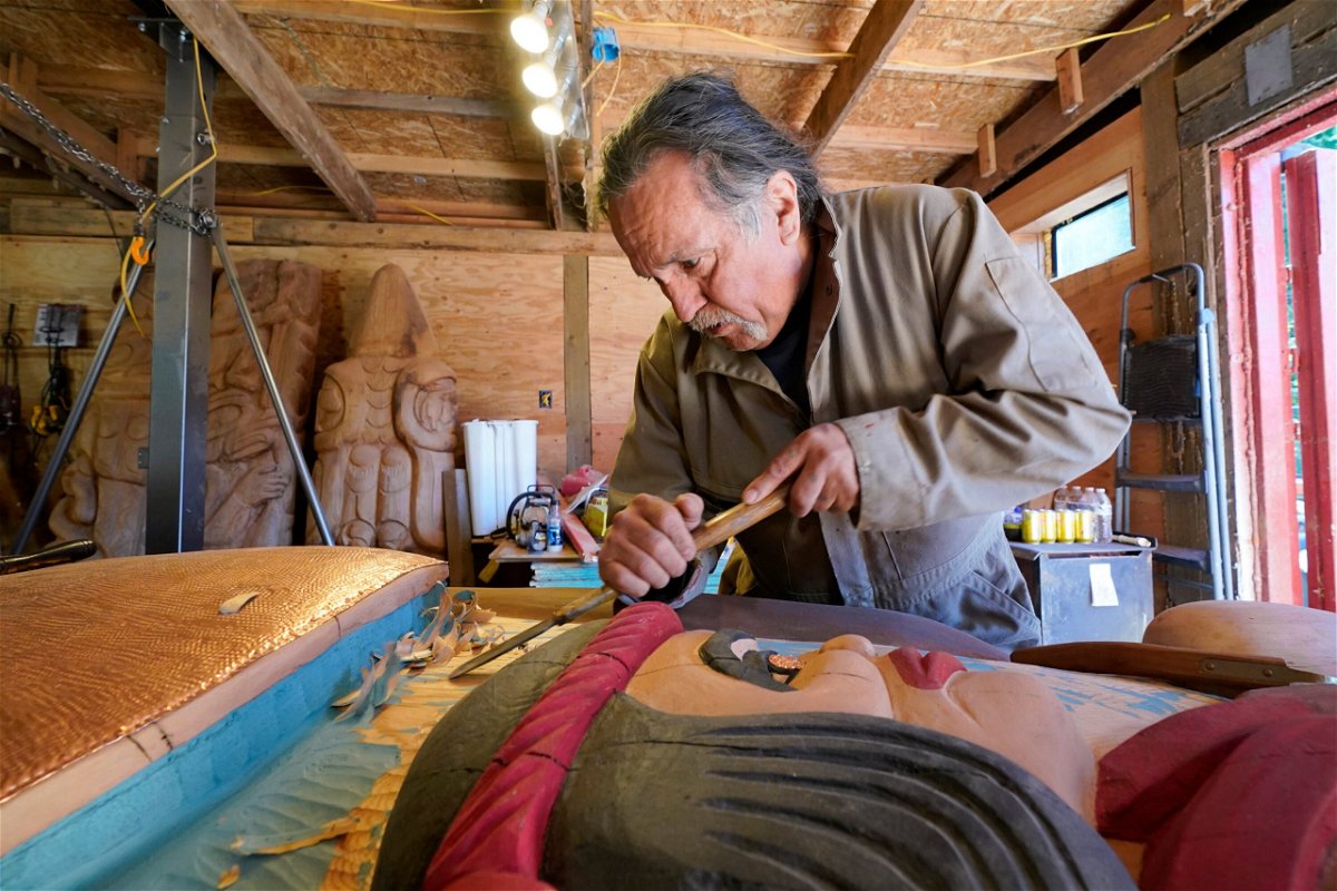 <i>Elaine Thompson/AP</i><br/>Lummi Nation lead carver Jewell James works on the final details of a nearly 25-foot totem pole to be gifted to the Biden administration at the end of July.