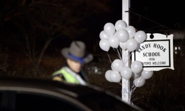 White balloons decorate the sign for the Sandy Hook Elementary School as a Connecticut State Trooper stands guard at the school's entrance in 2012 in Newtown