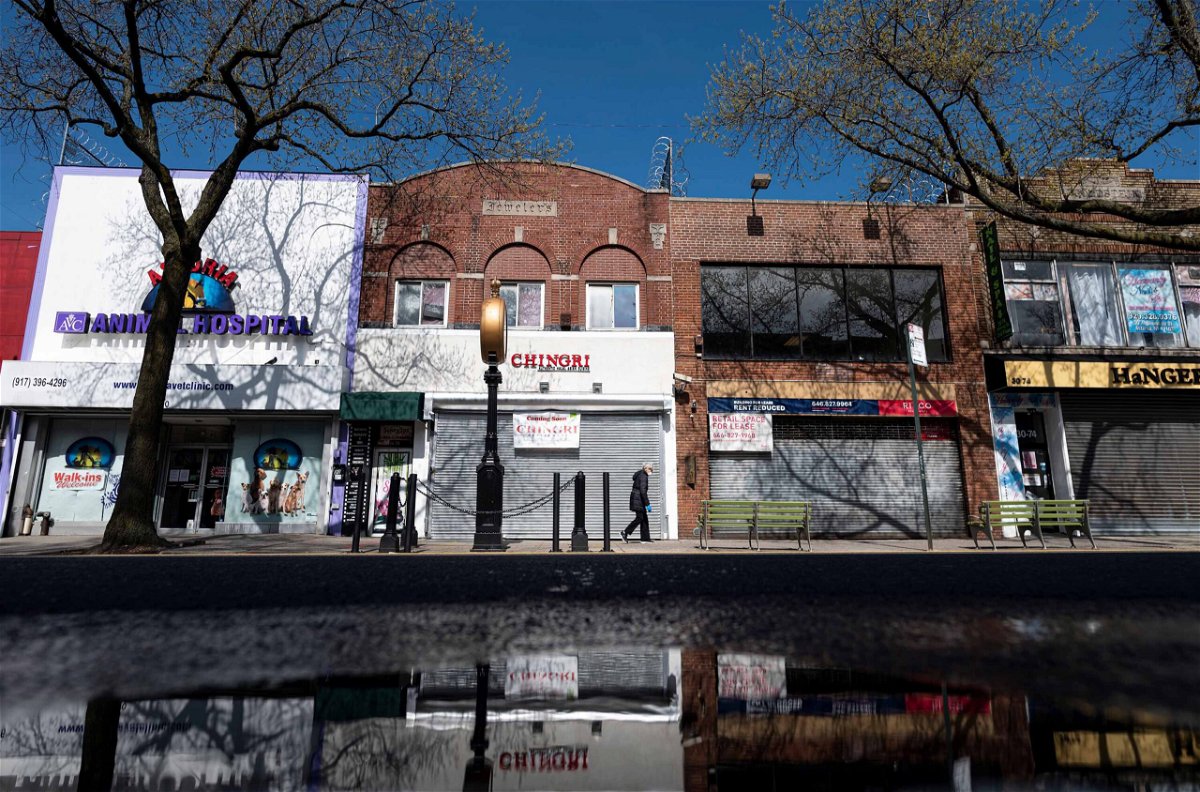 <i>JOHANNES EISELE/AFP/Getty Images</i><br/>A woman wearing a mask walks past closed storefronts in the Astoria neighborhood of Queens