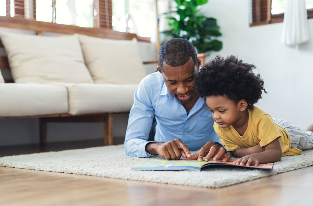 <i>Shutterstock</i><br/>A father and his son read a book while lying on the floor at home.
