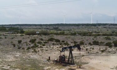 Blades from wind turbines rotate in a field behind an out-of-use oil pumpjack on April 16 near Eldorado