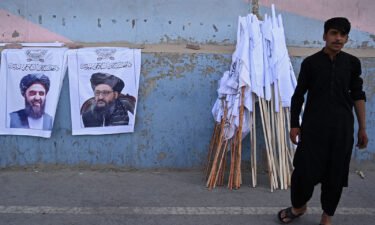 A vendor selling Taliban flags stands next to the posters of Taliban leaders Mullah Abdul Ghani Baradar and Amir Khan Muttaqi