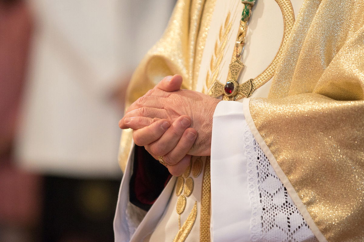 <i>Calamity Jane/Shutterstock</i><br/>A Catholic priest holds praying hands.