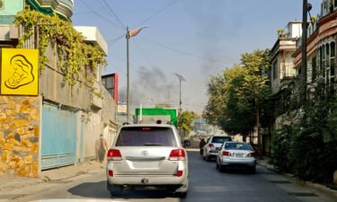 Vehicles move along a road against the backdrop of smoke rising from the site of blast in Kabul on November 2 after at least 16 people were wounded in two blasts at a military hospital.