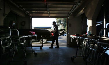 Funeral attendant Sam Deras helps wheel the casket of a person who died after contracting COVID-19 past gurneys toward a hearse at East County Mortuary on January 15