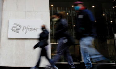 Shares of drug giant Pfizer surged more than 10% in early trading Friday after the company announced positive test results for an experimental pill it has developed to fight Covid-19. People are shown here walking in front of Pfizer sign at Pfizer World Headquarters on March 23