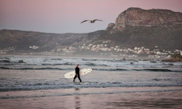 A surfer carries his board as he braves the cold waters at sunrise in Muizenberg
