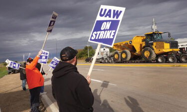 At truck hauls a piece of John Deere equipment from the factory past workers picketing outside of the John Deere Davenport Works facility on October 15