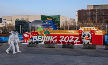 People in personal protective kits walking past a Winter Olympics display on Wednesday in Beijing.