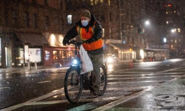 A food delivery driver on a bicycle rides in the snow on Friday in New York City.