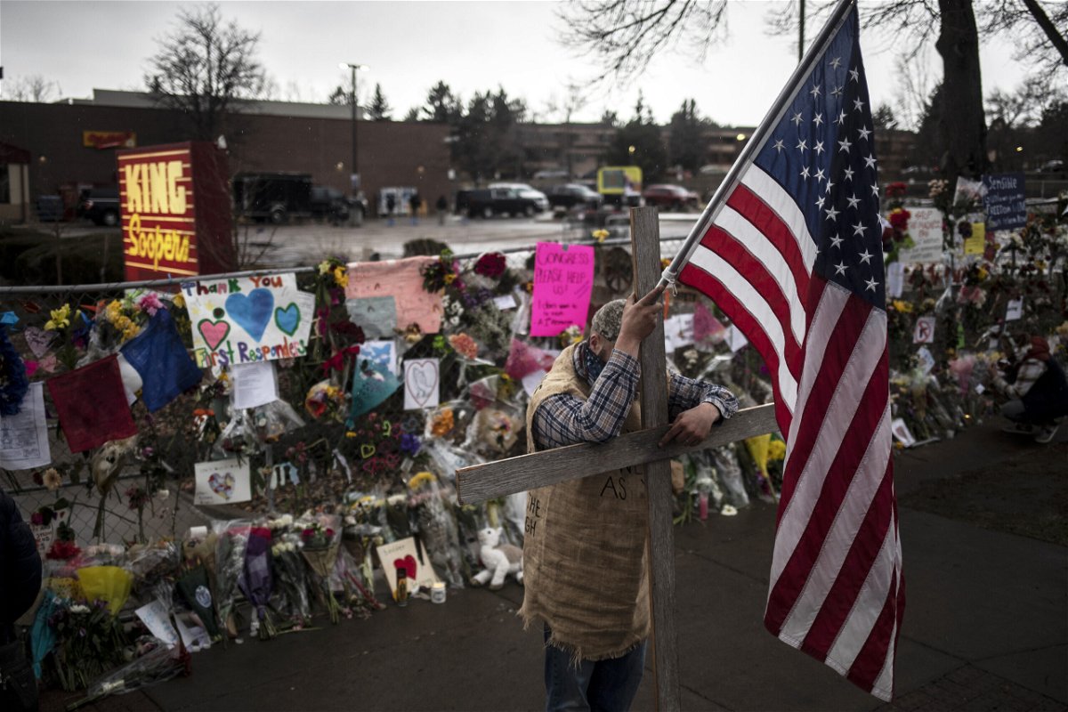 <i>Chet Strange/Getty Images</i><br/>A mourner leans on a cross while holding a flag outside a memorial at a King Soopers Grocery store on March 26