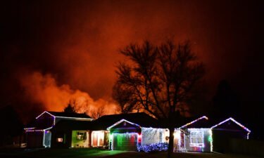 Christmas lights adorn a house as fires rage in the background as the Marshall Fire didn't ease during the nighttime hours.