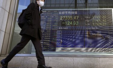 A pedestrian moves past a monitor showing Japan's Nikkei 225 index