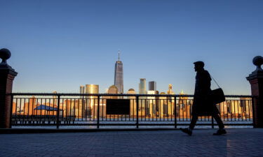 An evening commuter is silhouetted against the glistening New York City skyline at sunset as he walks along Hudson River shoreline in Jersey City