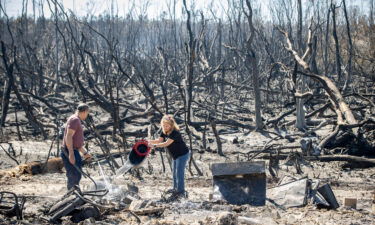 Hector Rivera and Wandi Blanco put water on hotspots on a neighbor's shed next to their home Saturday after the Adkins Fire tore through the area in Panama City