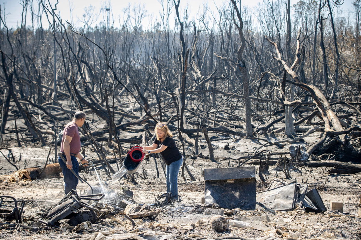 <i>MIKE FENDER/USA TODAY NETWORK/REUTERS</i><br/>Hector Rivera and Wandi Blanco put water on hotspots on a neighbor's shed next to their home Saturday after the Adkins Fire tore through the area in Panama City