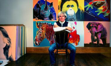 American Pop artist Andy Warhol sits in front of several paintings in his 'Endangered Species' at his studio