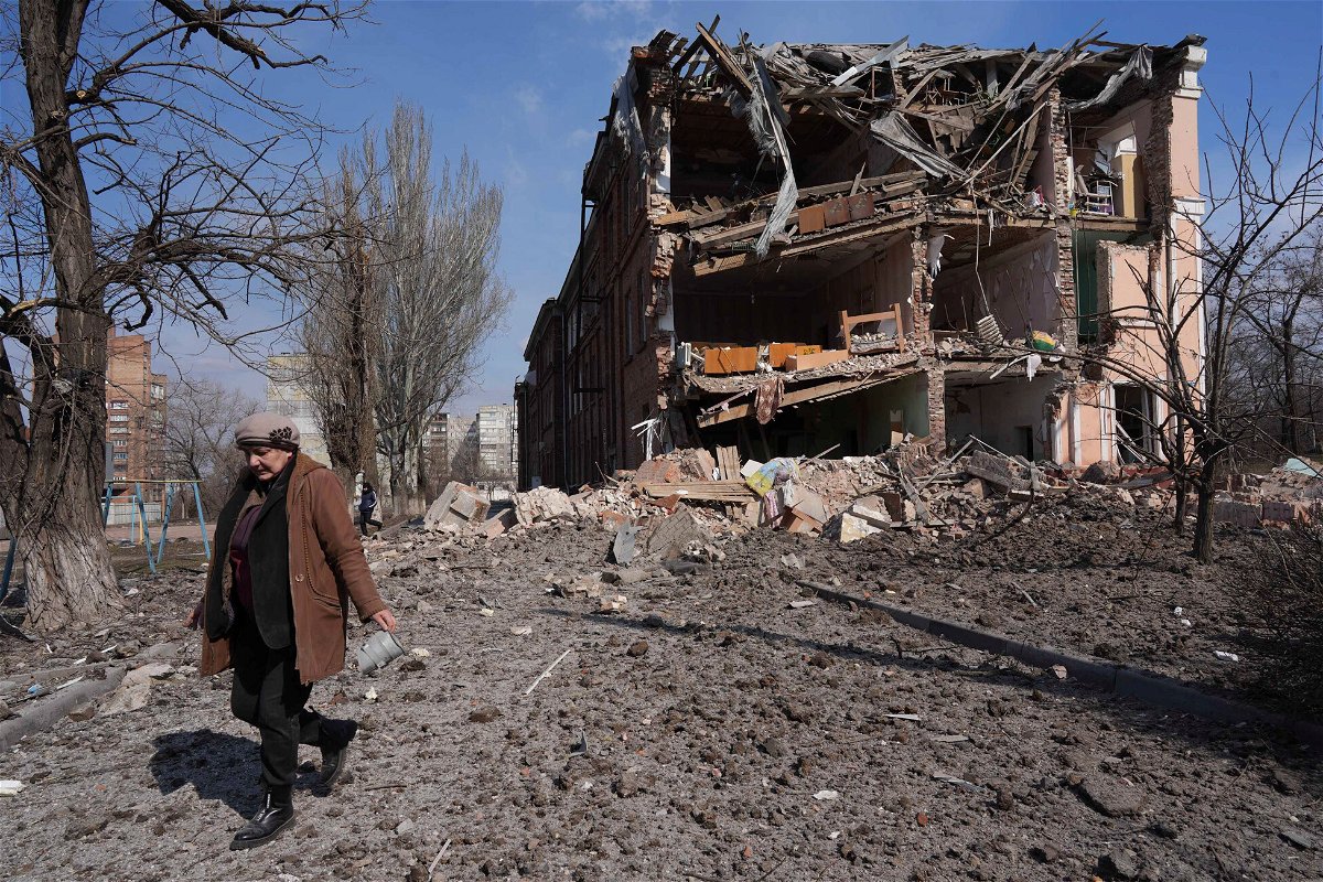 <i>Evgeniy Maloletka/AP</i><br/>A woman walks past building damaged by shelling in Mariupol on Sunday.