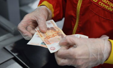 A cashier looks at a 5000 ruble banknote at a grocery shop of the Magnit food retailer. Magnit has announced it will hold the retail margin at 5% for a number of essential products.