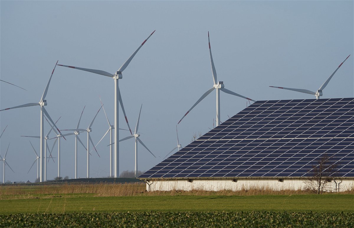 <i>Marcus Brandt/picture alliance/Getty Images</i><br/>Wind turbines stand next to a hall with photovoltaic systems on the roof in Schleswig-Holstein