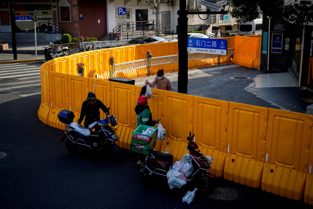 <i>ALY SONG/REUTERS</i><br/>Shanghai has said it will lock down each half of the city by turns for mass Covid-19 testing starting Monday amid surging infections. A delivery worker is shown here passing food to a woman over the barriers of an area under lockdown in Shanghai on March 23