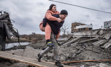 A man carries a woman as they cross an improvised path while fleeing the town of Irpin