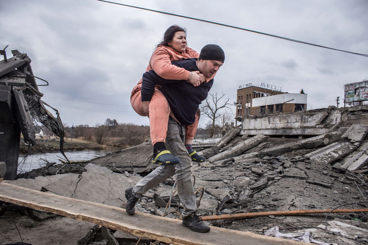 <i>Oleksandr Ratushniak/AP</i><br/>A man carries a woman as they cross an improvised path while fleeing the town of Irpin