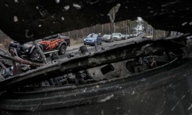 Cars drive past a destroyed Russian tank as a convoy of vehicles evacuating civilians leaves Irpin