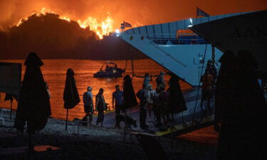 People board a ferry during evacuation as a wildfire burns in the village of Limni