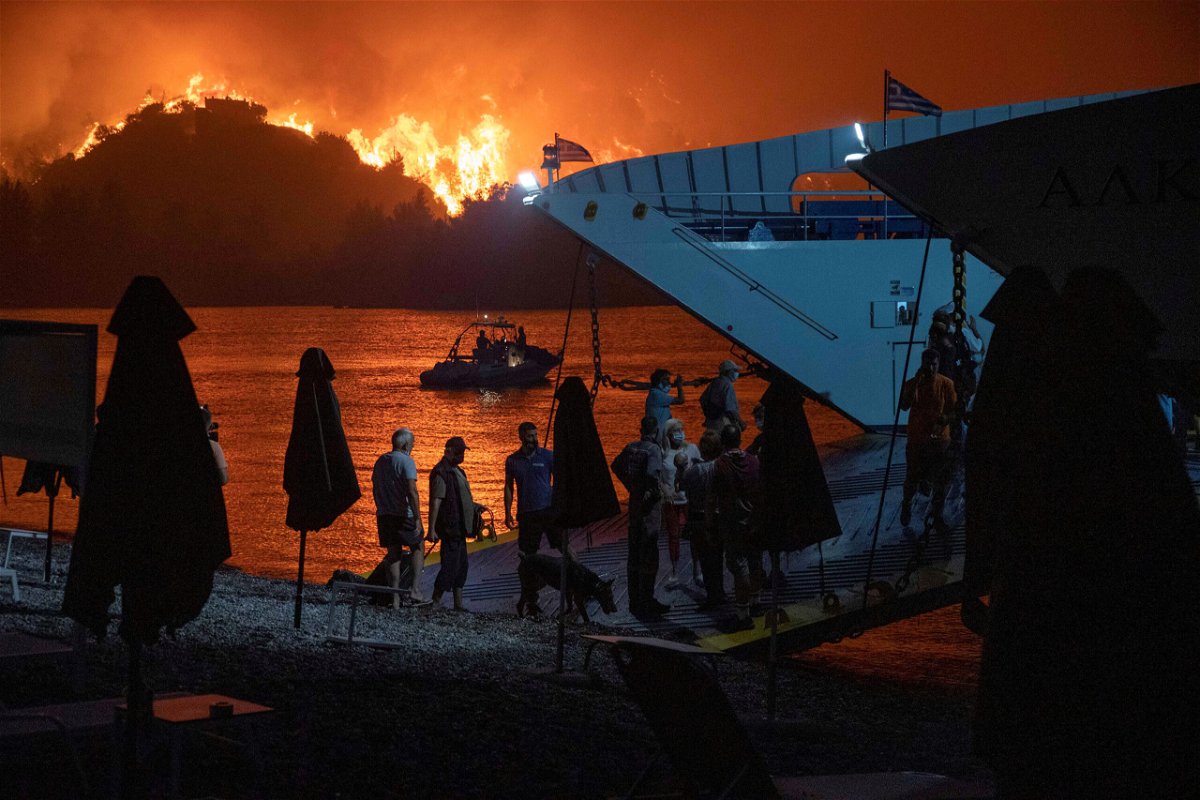 <i>Nicolas Economou/Reuters</i><br/>People board a ferry during evacuation as a wildfire burns in the village of Limni