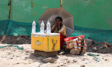 A girl selling water uses an umbrella to protect herself from the sun during a heat wave in New Delhi