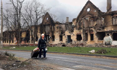 A woman pulls her bags past houses damaged in Mariupol