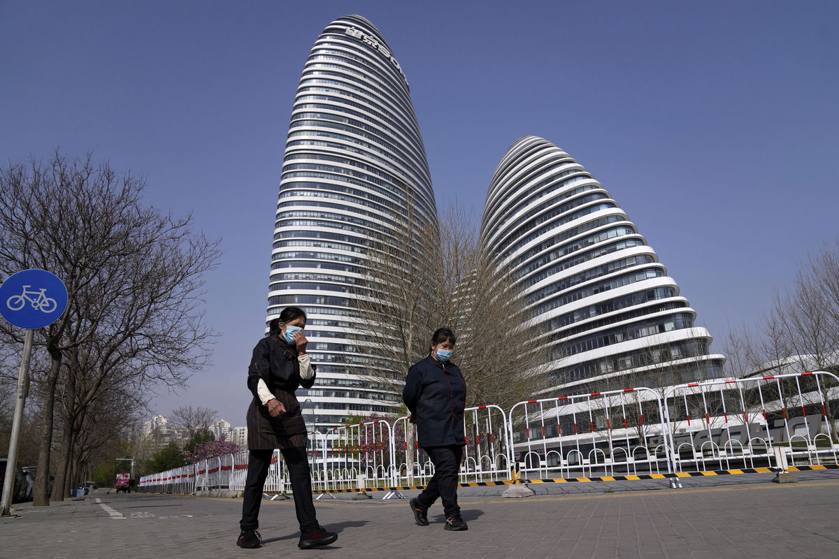 <i>Andy Wong/AP</i><br/>Women wearing face masks walk by an office building locked down for health monitoring on April 5 in Beijing