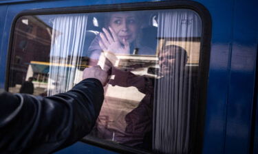 A woman waves to say good bye to her husband as she leaves on a bus