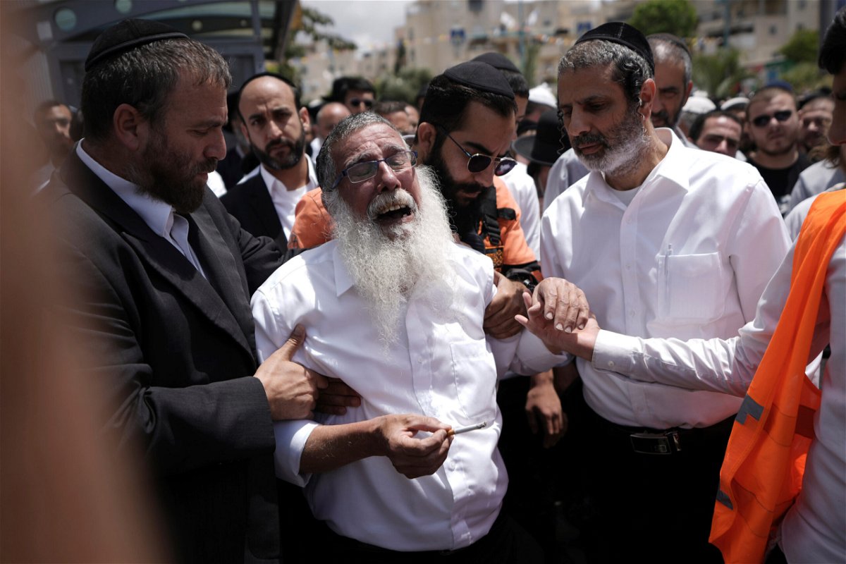 <i>Ariel Schalit/AP</i><br/>Ultra-Orthodox Jewish mourners encircle a man overcome with grief following the attack.