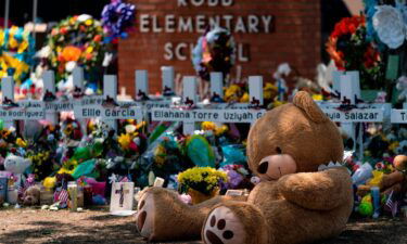 A teddy bear sits in front of crosses with the names of the 21 victims killed at Robb Elementary School.