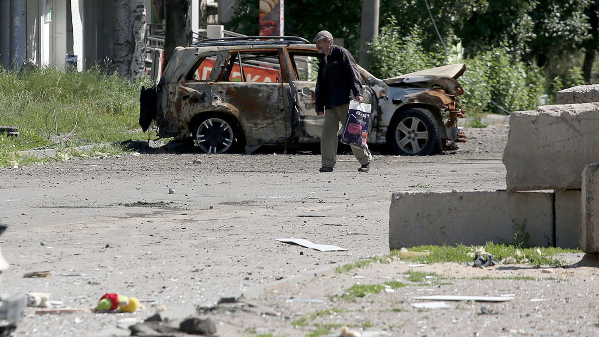 <i>ANATOLII STEPANOV/AFP/AFP via Getty Images</i><br/>A man walks past the wreckage of a car in Lysychansk on June 21