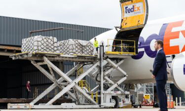 Workers unload a FedEx Express cargo plane carrying infant formula as a Secret Service agent stands watch at Dulles international airport in Dulles