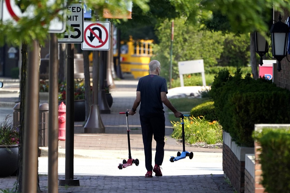 A man removes two children's scooters one day after a mass shooting in downtown Highland Park, Ill., Tuesday, July 5, 2022. A shooter fired on an Independence Day parade from a rooftop spraying the crowd with gunshots initially mistaken for fireworks before hundreds of panicked revelers of all ages fled in terror. 