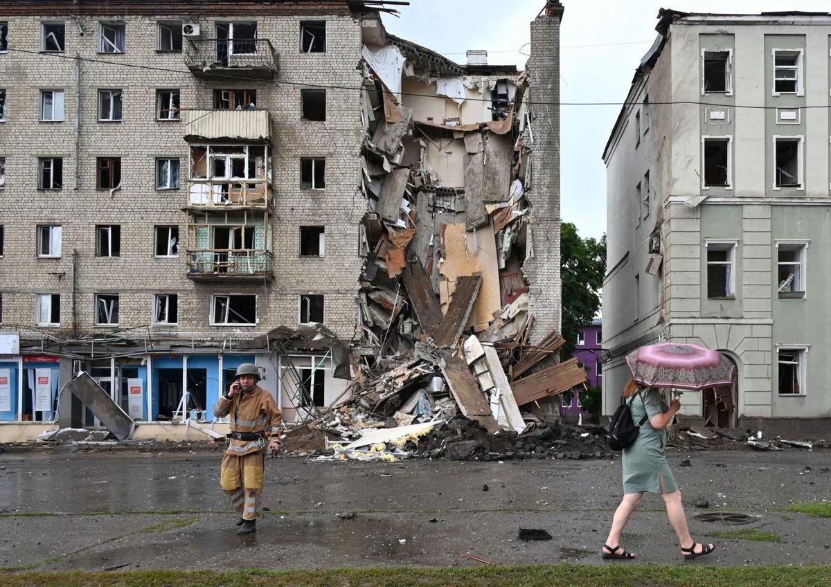 <i>SERGEY BOBOK/AFP/AFP via Getty Images</i><br/>A local resident walks past a Ukrainian rescuer working outside a building partially destroyed after a Russian missile strike in Kharkiv on July 11 amid Russia's military invasion launched on Ukraine.