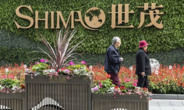 An elderly couple walk past a sign in front of Shimao Tower