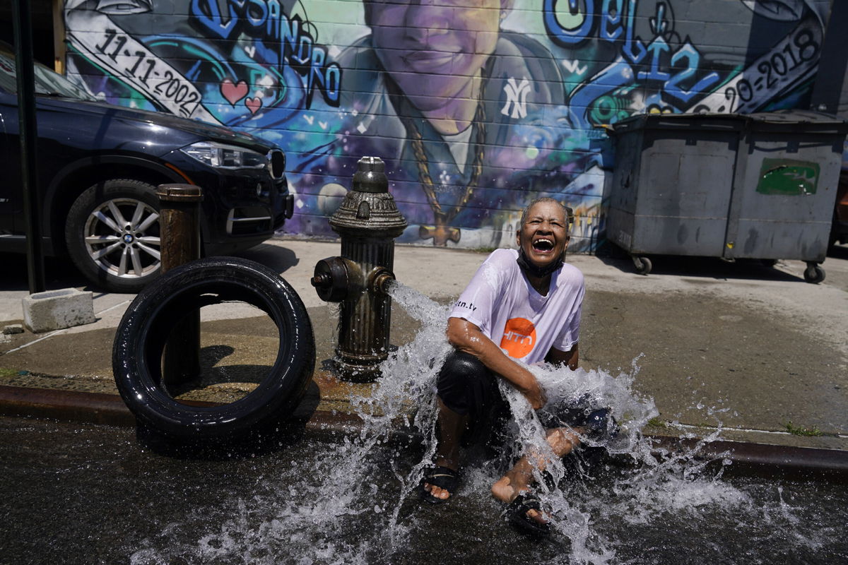 <i>Seth Wenig/AP</i><br/>Sylvia Carrasquillo reacts as she sits in front of an open fire hydrant Friday in The Bronx neighborhood of New York City.