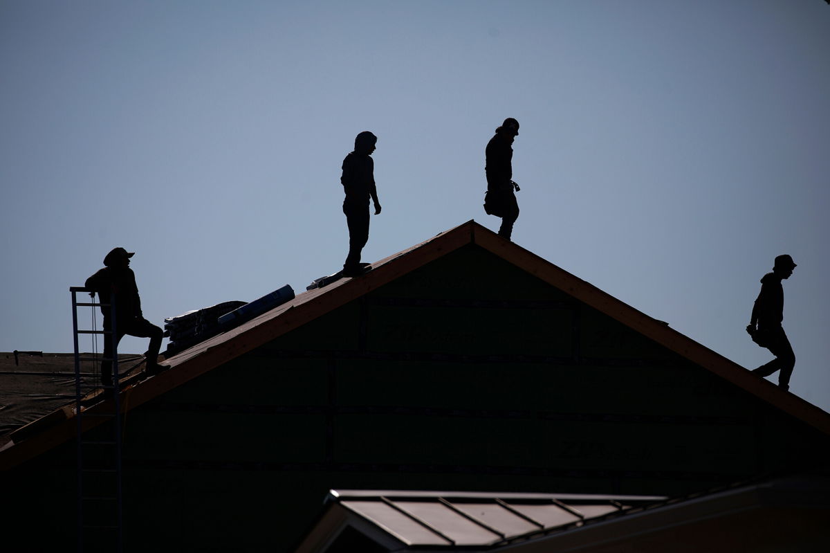 <i>Luke Sharrett/Bloomberg/Getty Images</i><br/>Contractors stand on the roof of a house under construction at the Norton Commons subdivision in Louisville