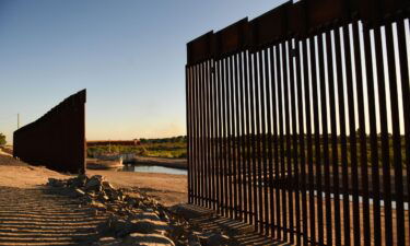 The sun sets behind a gap along the border wall at the Morelos Dam between the US and Mexico in Yuma